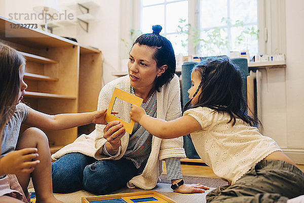 Female teacher and students holding picture frame while sitting in classroom at child care