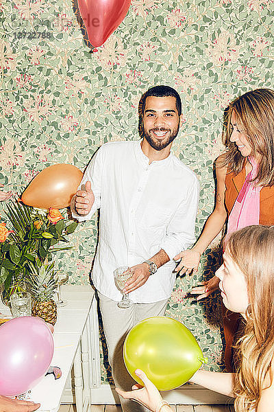 Portrait of smiling man standing with female friends and balloons at home during party