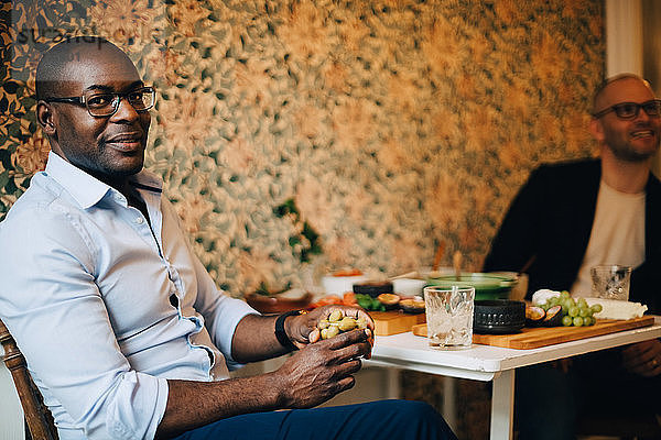 Portrait of man having food while sitting with friend by wall at home