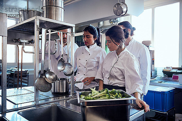 Chef team looking at colleague cooking food in commercial kitchen