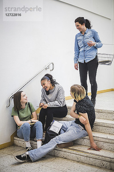 Smiling teacher looking at students sitting on steps at high school