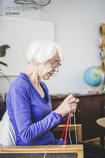 Senior woman knitting while sitting on chair in nursing home