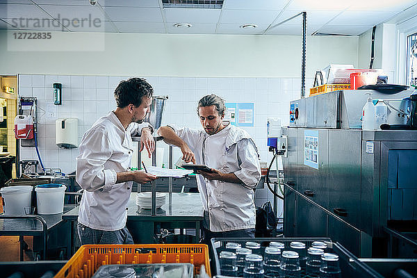Male chefs with digital tablet and documents in kitchen