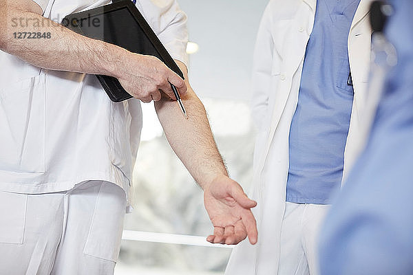 Midsection of male nurse gesturing while standing with coworkers at hospital