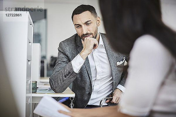Mid adult businessman discussing with female coworker while sitting in office