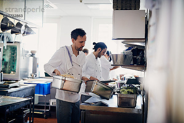 Young male chef carrying containers of food in commercial kitchen