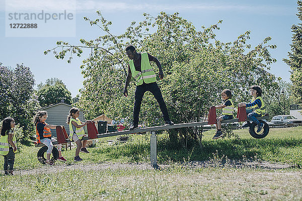 Full length of male teacher enjoying with students on seesaw in playground