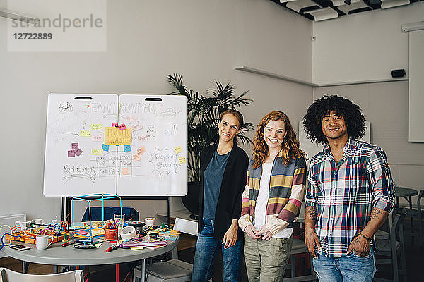 Portrait of smiling technician team standing by table and whiteboard at creative office