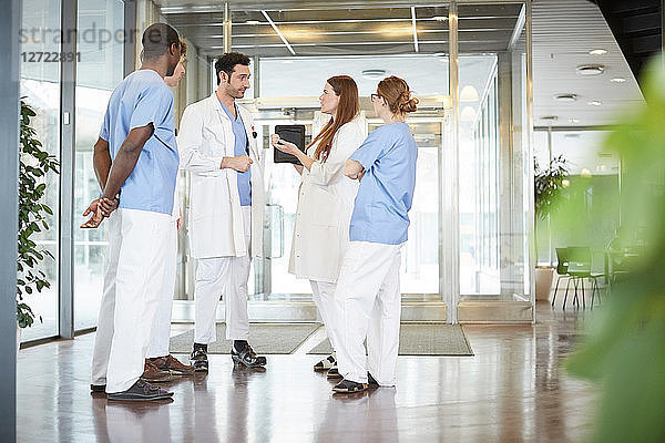 Full length of multi-ethnic healthcare team discussing while standing at lobby in hospital