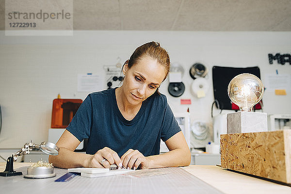 Confident female technician working at workbench while sitting in creative office