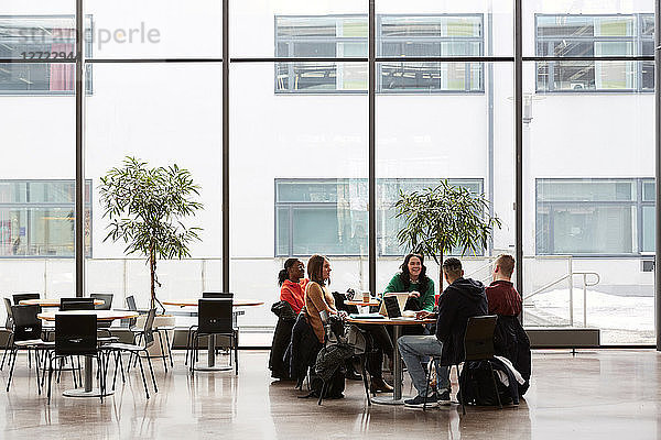 Full length of students talking while sitting at table in university