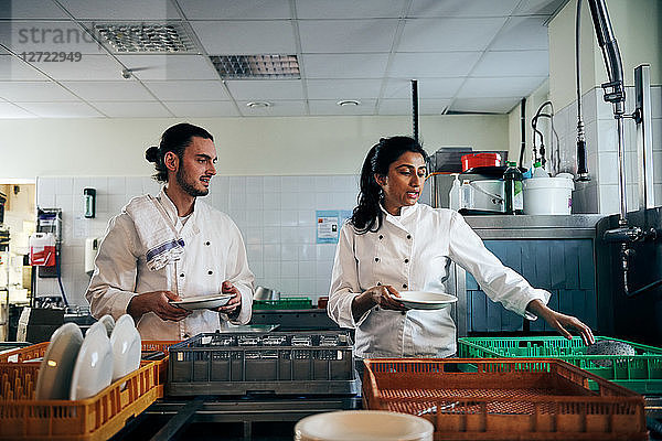 Male and female chefs communicating while holding plates in kitchen