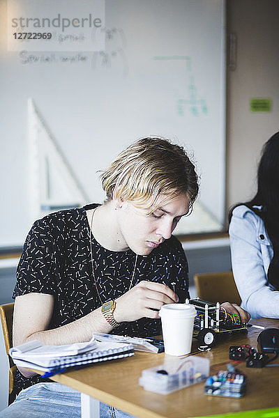 Confident young man making toy car on desk by friend in classroom at high school