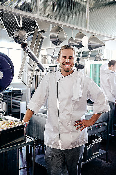 Portrait of smiling male chef standing with hand on hip in kitchen