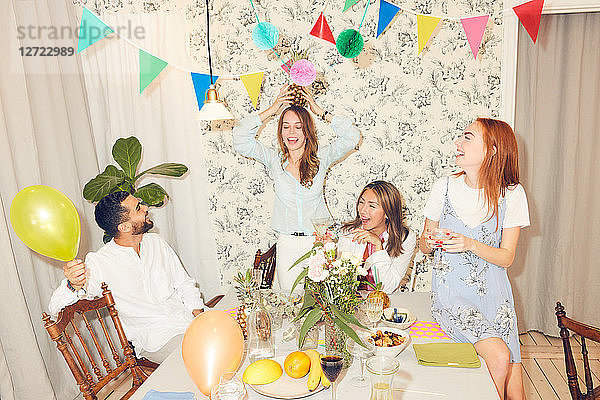 Young carefree friends playing with pineapple during dinner party at apartment