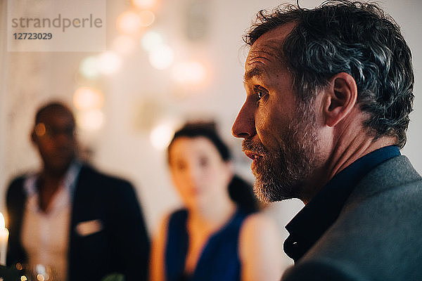 Close-up of mature man talking in dinner party with friends in background