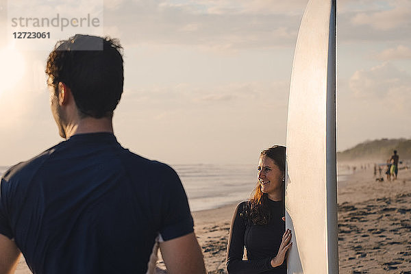 Young man with female friend holding surfboard at beach during sunset