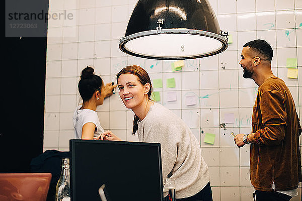 Smiling young businesswoman looking away while hackers planning over wall at small office