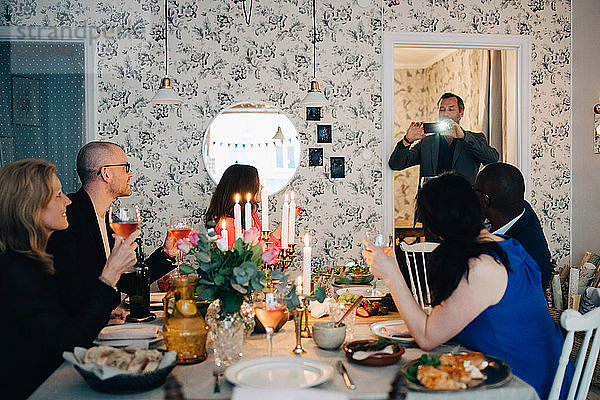 Man photographing mature friends at dinner party