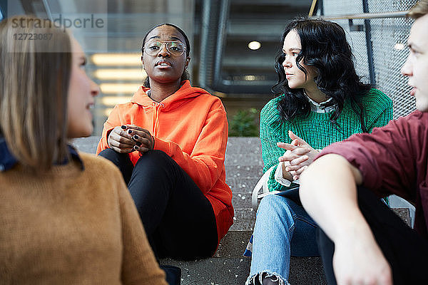 Multi-ethnic students talking while sitting on steps at university