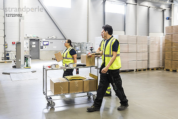 Multi-ethnic coworkers walking while pushing cart at distribution warehouse
