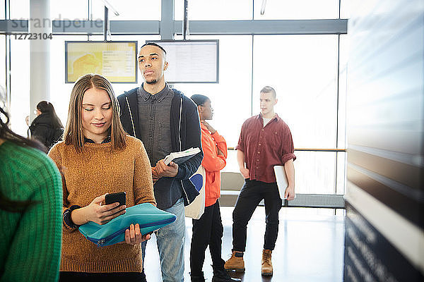 Young male and female students standing in row at university lobby