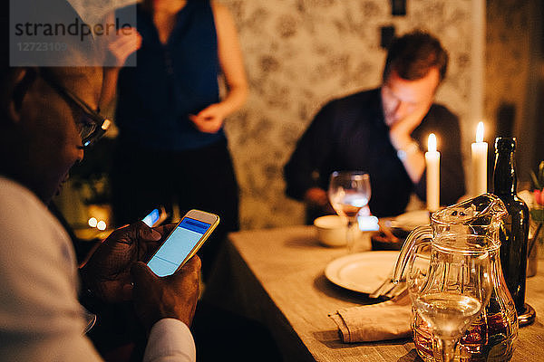 Mature man using mobile phone while having dinner with friends at party