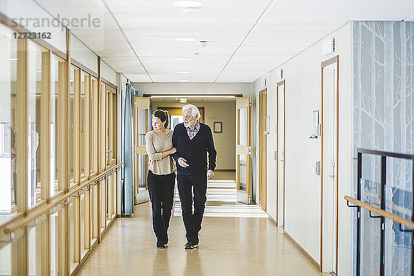 Young woman looking away while walking with grandfather in corridor at nursing home