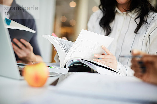 Midsection of friends studying with books at table in university