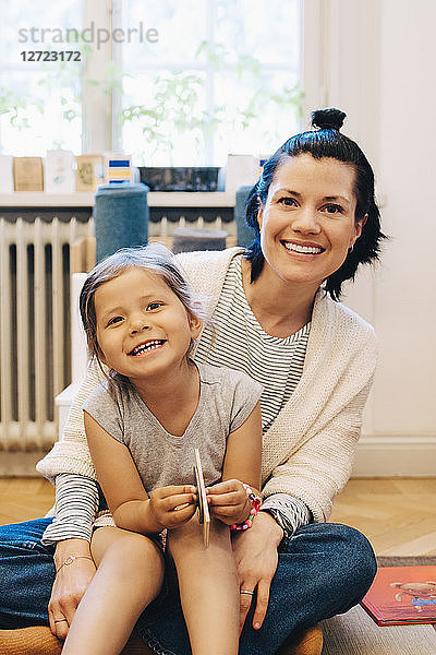 Portrait of smiling girl sitting on teacher's lap in kindergarten classroom