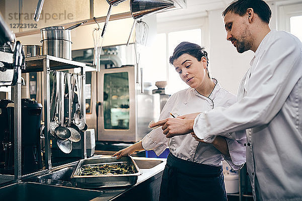 Male and female chefs reading order ticket while preparing food in commercial kitchen