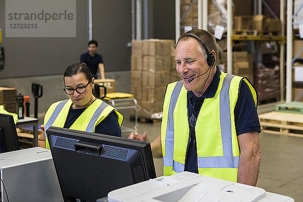 Confident senior male customer service representative talking through headset while standing by coworker in distribution