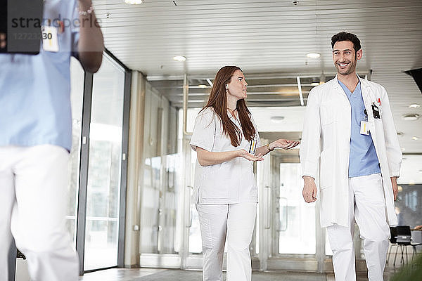 Smiling young healthcare workers discussing while walking in lobby at hospital