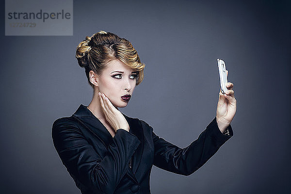 Porträt einer jungen Frau im Profil  die ein Foto mit ihrem Mobiltelefon macht
