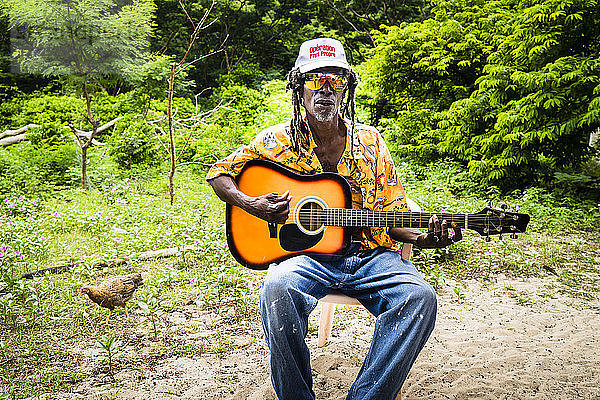 Rasta-Mann spielt Gitarre draußen in der Natur  Chatham Bay  Union  St-Vincent  St. Vincent und die Grenadinen  Kleine Antillen  Westindische Inseln  Inseln über dem Winde  Karibik  Mittelamerika