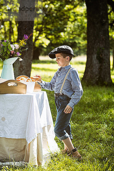 Kleiner Junge mit einem Schokoladencroissant in der Hand bei einem Brunch auf dem Land. Obligatorischer Kredit: Design culinaire : food-design-studio.fr