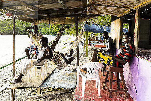Junge Leute sitzen unter einer Hütte und schauen auf das Meer  Chatham Bay  Union  St-Vincent  St. Vincent und die Grenadinen  Kleine Antillen  Westindische Inseln  Inseln über dem Winde  Karibik  Mittelamerika