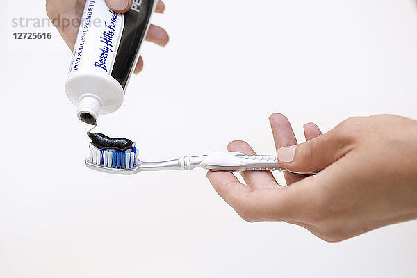 Detail Hände setzen Zahnpasta Aktivkohle auf eine Zahnbürste.