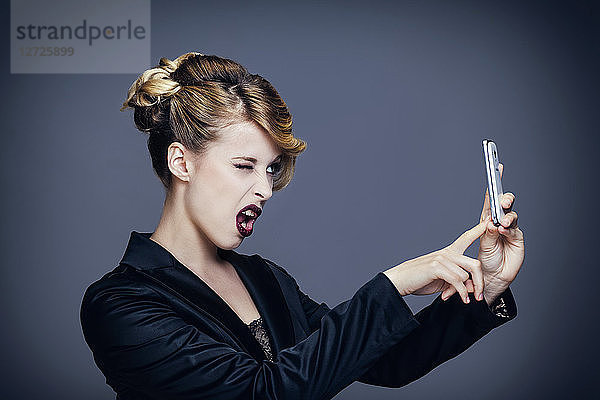Porträt einer jungen Frau  die im Profil zwinkert und ein Foto mit ihrem Mobiltelefon macht
