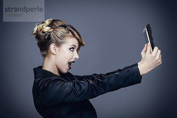 Porträt einer jungen Frau im Profil  die mit ihrem Touchpad fotografiert