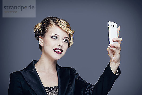 Porträt einer jungen Frau im Anzug  die mit ihrem Mobiltelefon Fotos macht