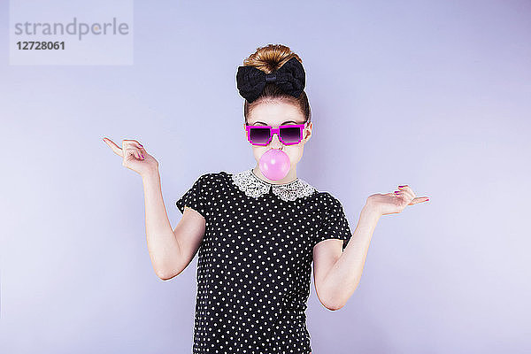 Humorvolles Porträt einer jungen Frau  die eine Kaugummiblase macht Hände an den Seiten