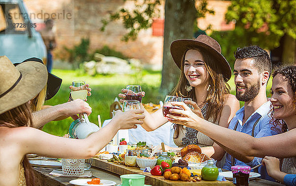 Planen Sie eine Gruppe von jungen Leuten  die bei einem Brunch auf dem Land sitzen und ihre Gläser erheben. Obligatorischer Kredit: Design culinaire : food-design-studio.fr