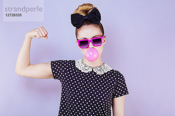 Humorvolles Porträt einer jungen Frau  die eine Kaugummiblase macht und ihren Bizeps zeigt
