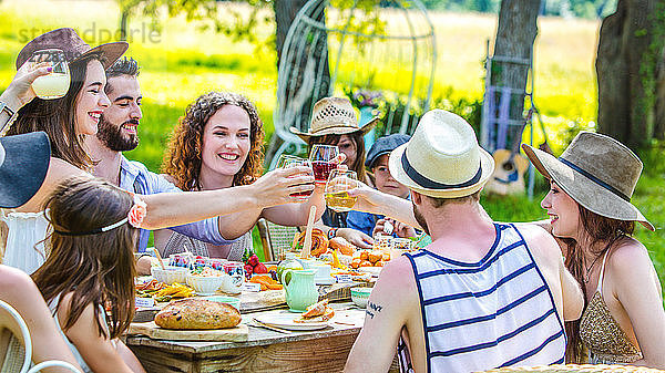 Eine Gruppe junger Leute  die bei einem Brunch auf dem Lande sitzen  erheben ihre Gläser. Obligatorischer Kredit: Design culinaire : food-design-studio.fr