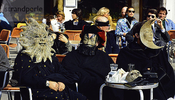 Europa  Italien  Karneval in Venedig. Drei maskierte Figuren sitzen in einem Café im Freien