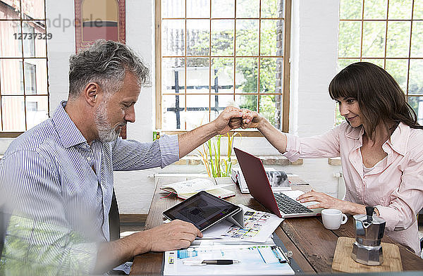 Mature couple high fiving in home office  using laptop and digital tablet