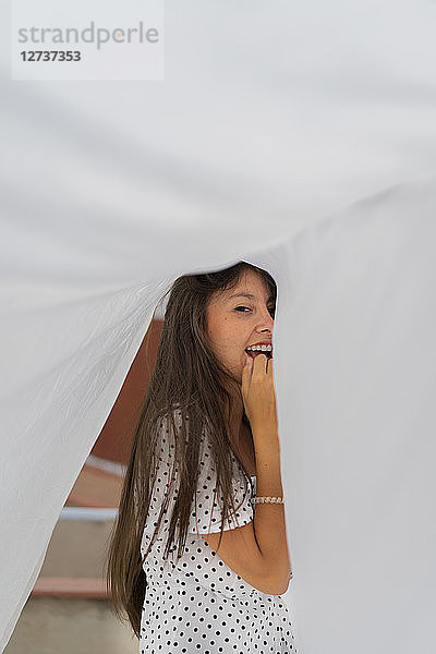 Portrait of young woman under drying bed sheet on roof terrace