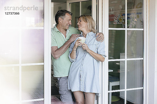 Happy mature couple standing at French window