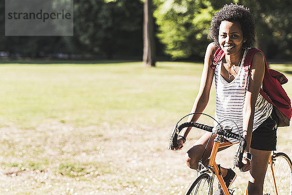 Portrait of smiling young woman on bicycle in park